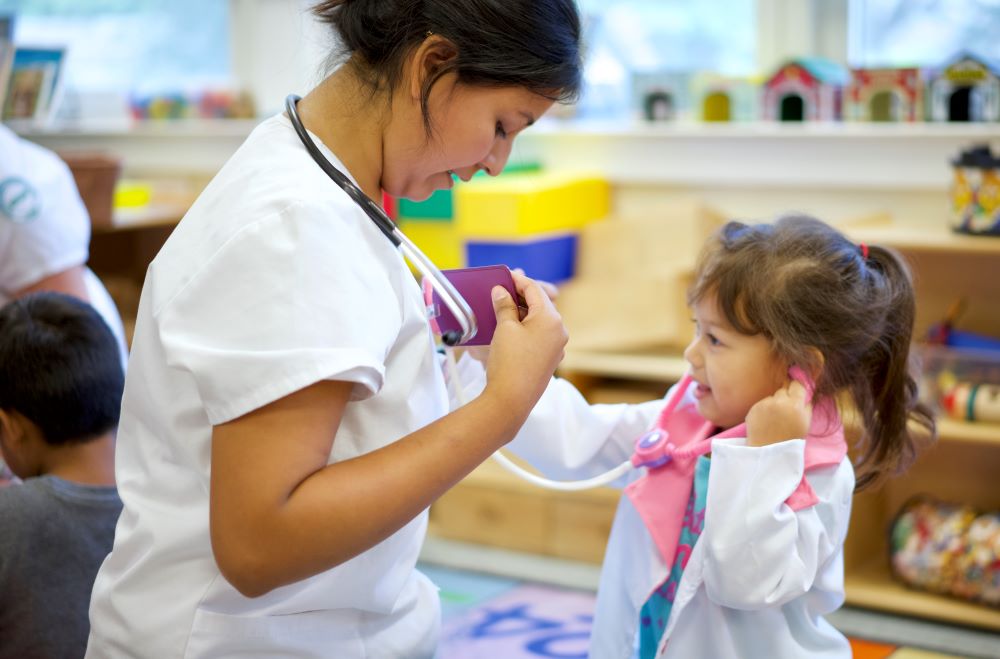 Una niña usando un estetoscopio de juguete para escuchar los latidos del corazón de un adulto.