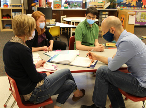 A group of adults sitting at a child-sized table going over their notes.