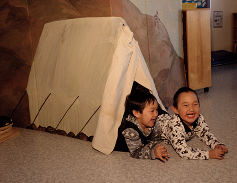 Two children inside a blanket tent.