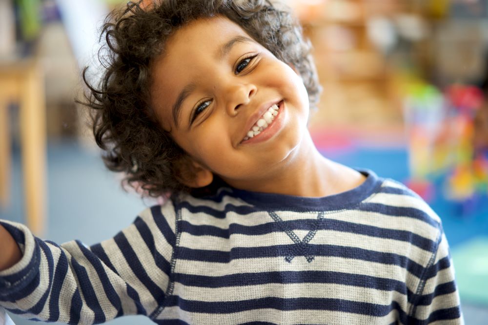 Un niño pequeño sonriente con la cabeza inclinada hacia un lado.