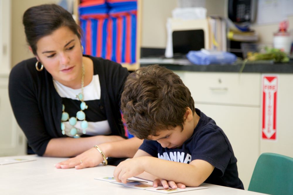 Una maestra observa a un niño que trabaja en una tarea difícil.