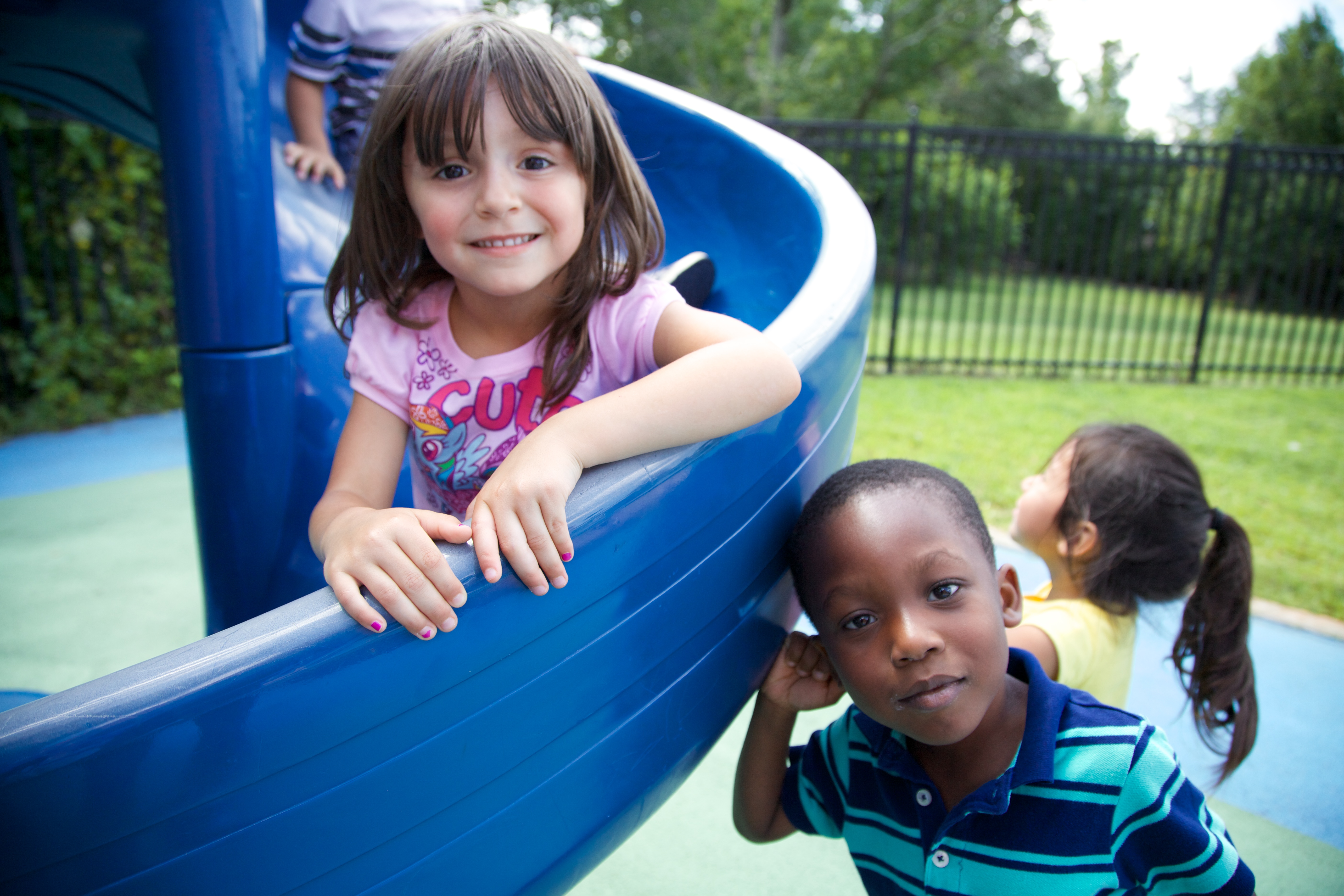 A young girl smiles at us from the top of a slide.