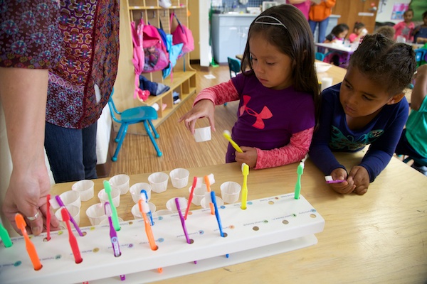 Two children setting up a tray full of toothbrushes and cups of water.