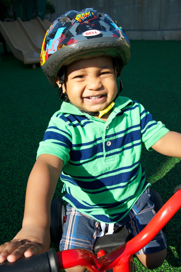 Young boy smiling as he rides his bicycle while wearing a helmet.