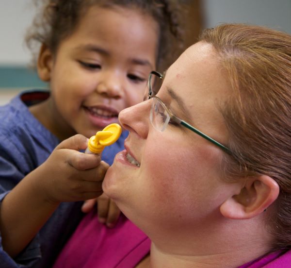 Niña revisando los dientes de una maestra con un espejo dental de juguete.