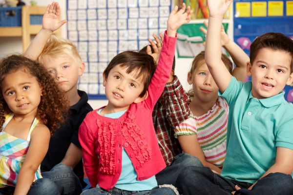 Niños sentados en el suelo y levantando las manos.