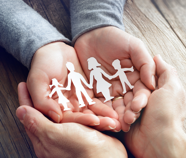 Child's open hands showing cutout people as a family unit holding hands.