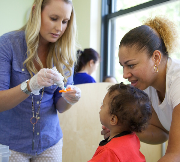 Asistente dental mostrándoles a una madre y su hijo cómo aplicar la pasta de dientes.