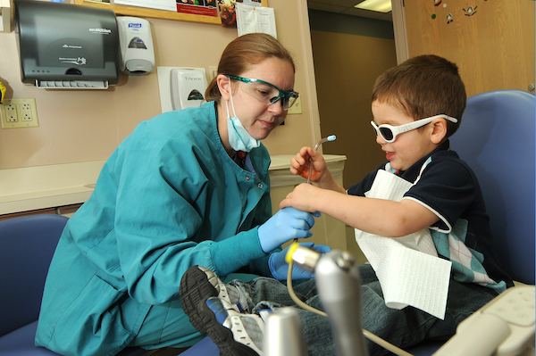 A boy wearing safety goggles being shown the tools a dentist is using.