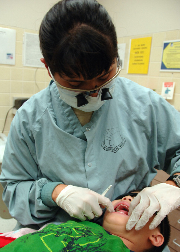 Dentist wearing goggles examing a child's mouth and teeth.