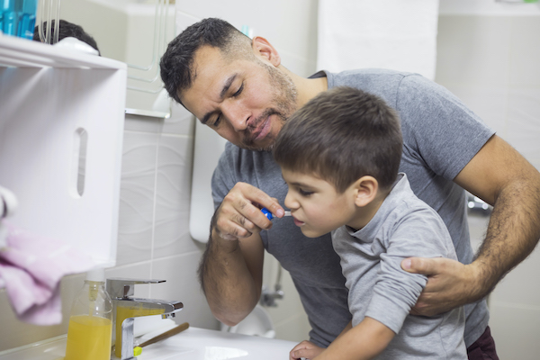 Father holding his son up to the sink so he can brush his teeth.