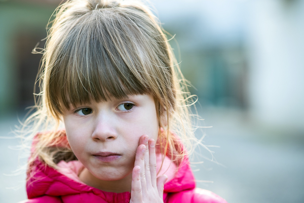 Young girl pressing on her left cheek because of a toothache.