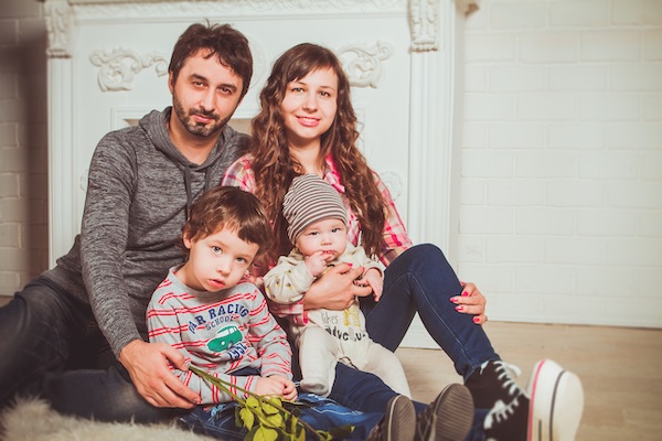 Mamá y papá con sus dos hijos pequeños sentados en el suelo mirando a la cámara.