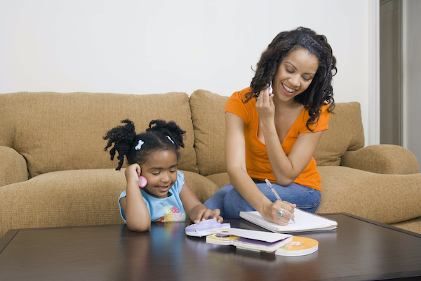 Madre e hija escribiendo y leyendo en la mesa frente al sofá.