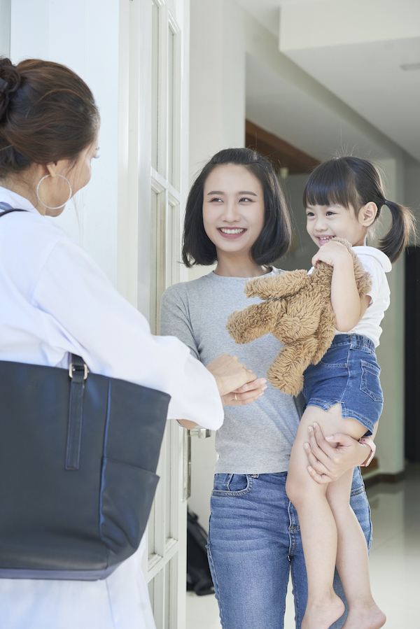 Madre e hija saludando a una visitadora del hogar en la puerta principal.