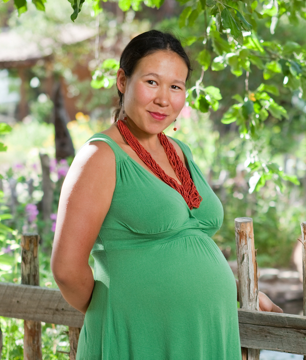 A smiling pregnant woman wearing a green dress.