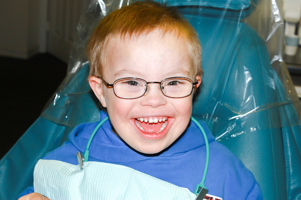 Niño con lentes sonriendo, en la silla del dentista.