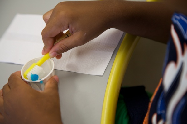 Maestra aplicando pasta de dientes en varios cepillos de dientes.