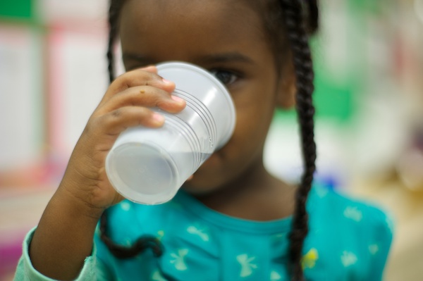 Young girl drinking water from a paper cup.