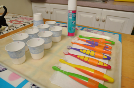 Una bandeja con varios cepillos de dientes de colores y vasos pequeños con enjuague bucal.