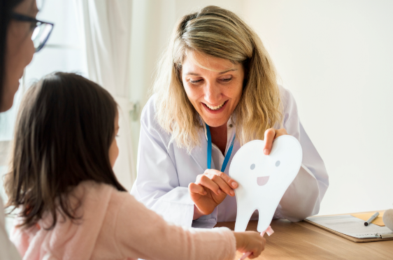 Dentista mostrándole a un niño un diente de cartón grande.