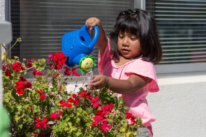 Young girl watering plants with a colorful watering can.