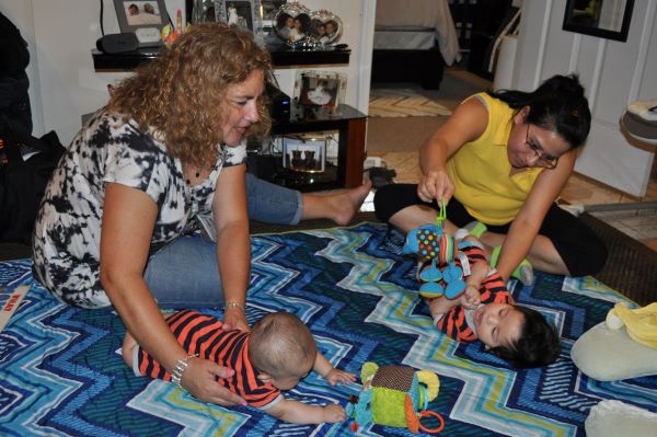 Two women sitting on the floor caring for two infants.