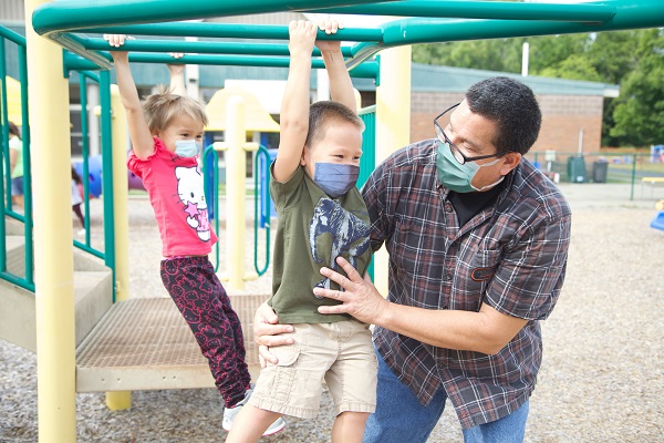 Boy hanging from monkey bars with teacher's assistant