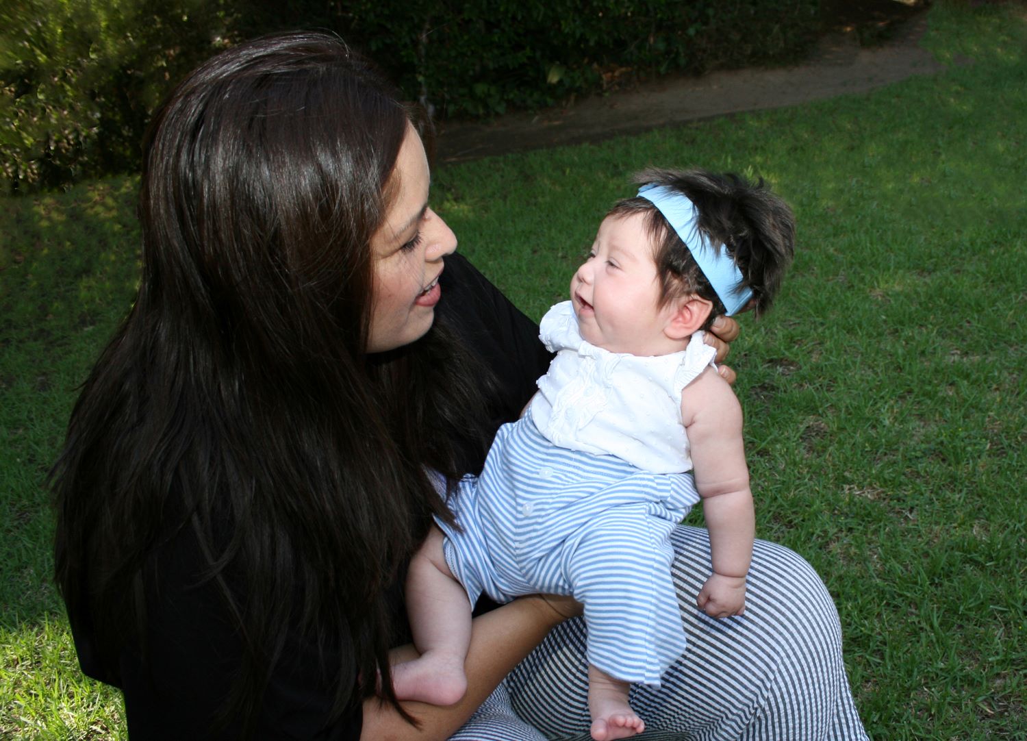 Mother holding her young child who is wearing a white bow on her head.