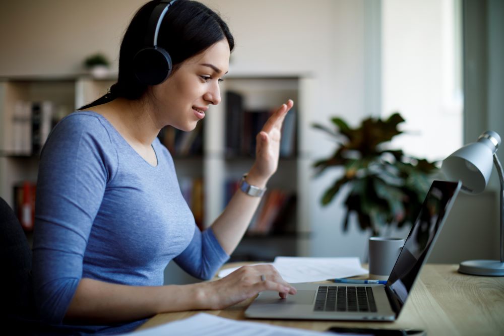 Mujer con auriculares usando una computadora portátil para participar en una reunión virtual por video.