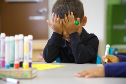 Child at a table with palms over his eyes as if giving up on a school task.