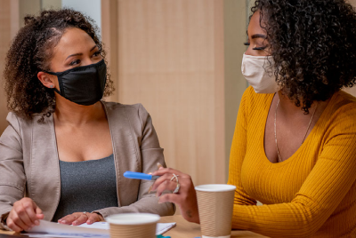 Two women using masks, meeting at a table.