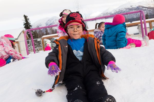 Child sitting down and sliding down a snowy hill.