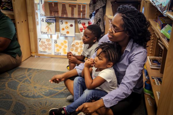 Teacher sitting on floor supporting a toddler.