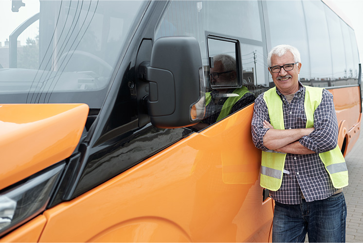 Bus driver wearing an orange safety vest standing beside his school bus.