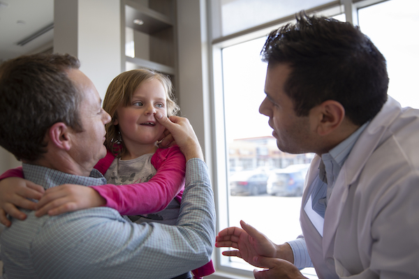 Father holding up his daughter while dentist talks to her.