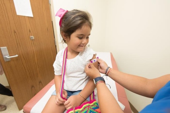 Young girl getting a colorful bandage on her left arm after being vaccinated.