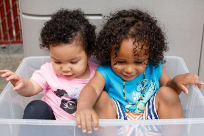 Dos niñas pequeñas divirtiéndose dentro de un recipiente de plástico grande.