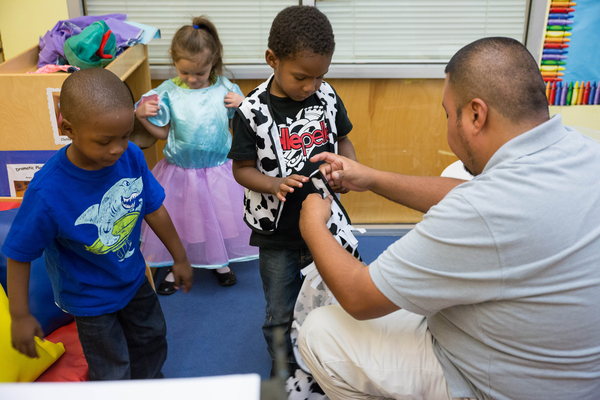 A teacher adjusting costumes for some children.