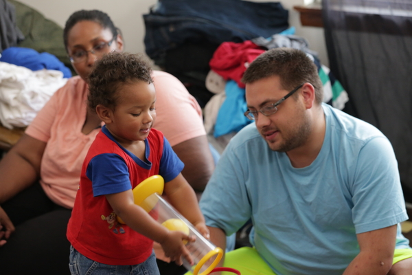 A man looks on as a young boy handles a large toy.