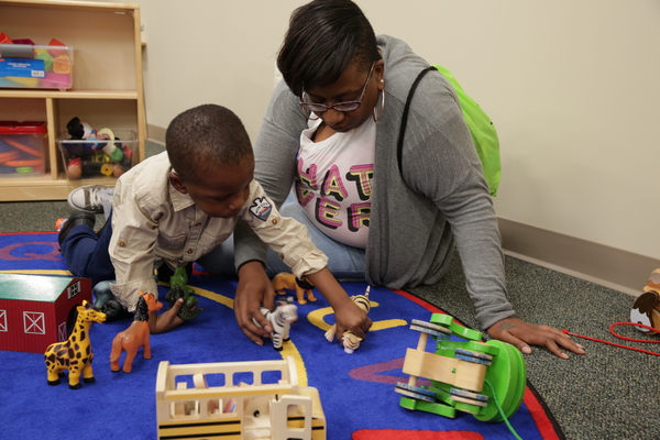 Teacher and young boy playing with wooden vehicles.