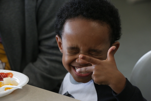 Niño entrecerrando los ojos y sonriendo mientras hace gestos con los dedos