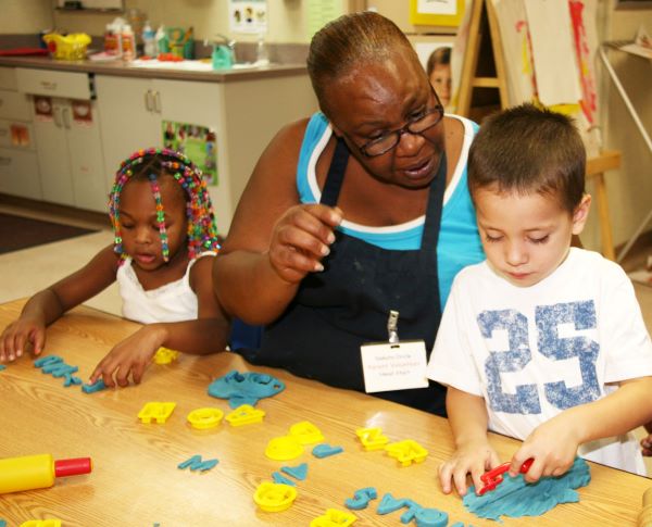 African-american teacher talking in a classroom with a boy, while a girl to her right sorts some letters.