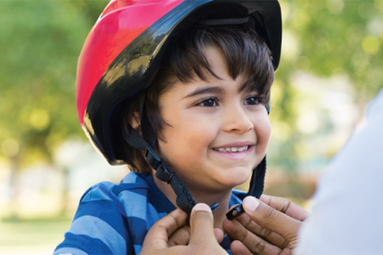 Adulto ayudando a un niño a atarse el casco de la bicicleta.