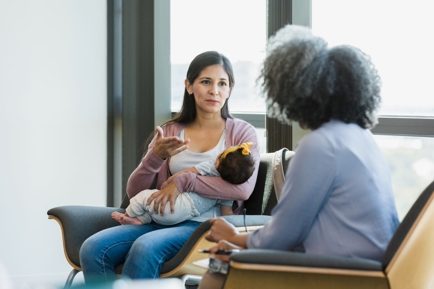 A mother cradling her infant daughter while speaking to a woman.