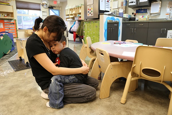 Teacher hugging a distressed child in a classroom.