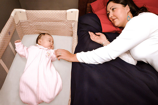 Baby sleeping in her crib, next to her caregiver.