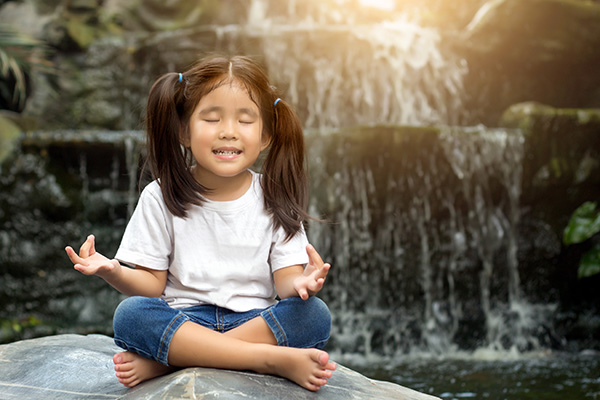 Niña meditando y haciendo la postura de loto.