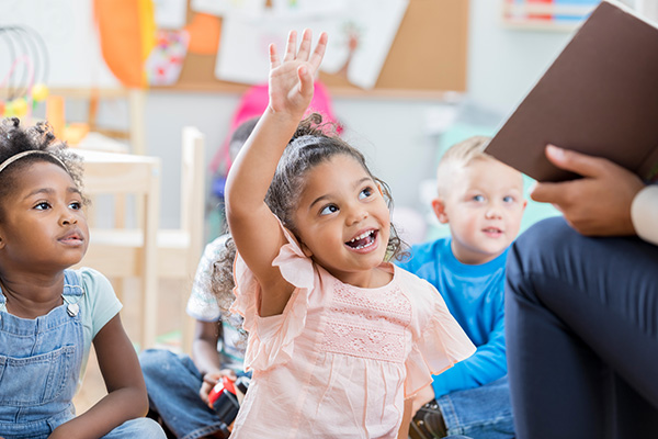 Child smiling and rising a hand at circle time.