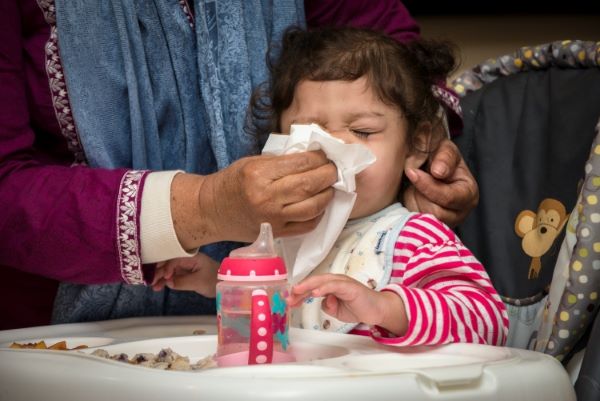 Child sitting at a table while being blown her nose.